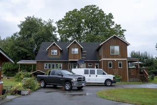 Hunter Green Interlock Slate aluminum roof on a brown two-storey home with dormers among tall pines, Langley, British Columbia