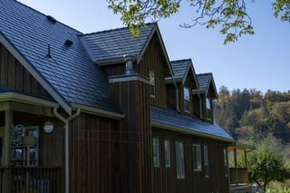 Hunter Green Interlock Slate aluminum roof on a brown chalet-style home with dormers in a forested rural, Langley, British Columbia