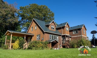Large two-storey farmhouse with hunter green Interlock aluminum slate metal roofing, multiple dormers, and warm cedar board-and-batten siding in Langley, BC.