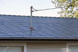 Deep Charcoal Interlock Slate aluminum roof on a beige single-family home with a metal roof in a forested, Mission, British Columbia