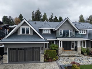 Deep Charcoal Interlock Slate aluminum roof on a grey home with stone accents among tall trees in the, North Vancouver, British Columbia