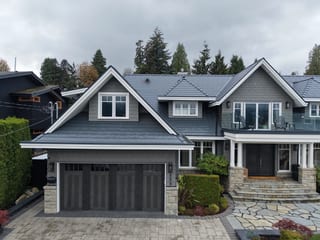 Deep Charcoal Interlock Slate aluminum roof on a grey two-storey home with dormers among tall pines, North Vancouver, British Columbia