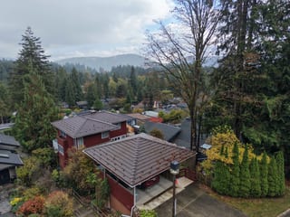 Colonial Brown Interlock Shake aluminum roof on a red two-storey home with a brown metal roof among tall, North Vancouver, British Columbia