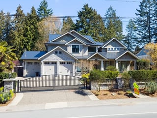 Large Craftsman home in Tsawwassen BC with dark black Interlock cedar-shingle metal roof featuring multiple gables, dormers, and stone accents behind iron gate.
