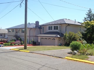 Black Interlock Slate aluminum roof on a beige two-storey home with a metal roof among greenery, Victoria, British Columbia