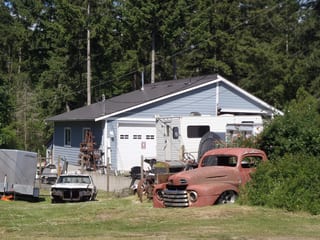 Weathered Interlock Slate aluminum roof on a blue single-family home with a garage in a forest clearing, Duncan, British Columbia