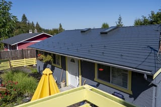 Deep Charcoal Interlock Slate aluminum roof on a dark grey one-storey home with a metal roof in a forested, Ladysmith, British Columbia