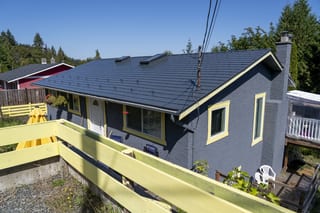Deep Charcoal Interlock Slate aluminum roof on a two-storey home with a dark grey metal roof among tall, Ladysmith, British Columbia