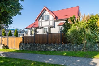 Tile Red Interlock Slate aluminum roof on a white Tudor style home with dormers among tall trees, Victoria, British Columbia