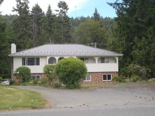 Tudor Brown Interlock Cedar Shingle aluminum roof on a Tudor style home with a brown metal roof among tall trees, Ladysmith, British Columbia