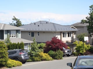 Deep Charcoal Interlock Slate aluminum roof on a tan two-storey home with a metal roof among green shrubs, Victoria, British Columbia