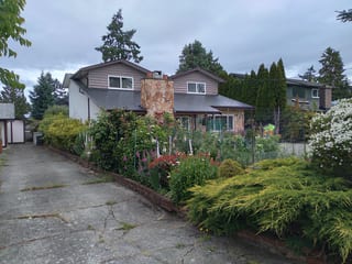 Black Interlock Slate aluminum roof on a two-storey home with a metal roof among trees and shrubs, Victoria, British Columbia