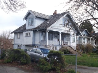 Tudor Brown Interlock Cedar Shingle aluminum roof on a light grey two-storey Tudor home with dormers and a metal, Victoria, British Columbia