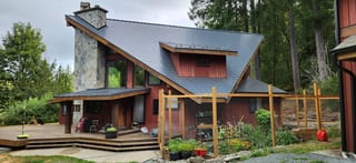 Deep Charcoal Interlock Slate aluminum roof on a red chalet-style home with a metal roof among tall trees, Shawnigan Lake, British Columbia