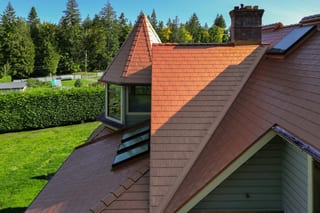 Copper Penny Interlock Slate aluminum roof on a two-storey home with dormers in a wooded rural setting, Ladysmith, British Columbia