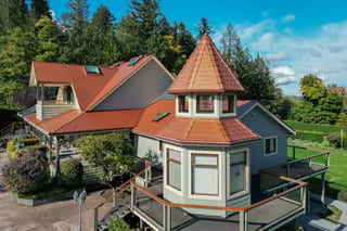 Copper Penny Interlock Slate aluminum roof on a grey single-family Craftsman home with dormers among tall, Ladysmith, British Columbia