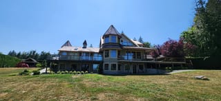Copper Penny Interlock Slate aluminum roof on a brown two-storey home with dormers among tall pines, Ladysmith, British Columbia