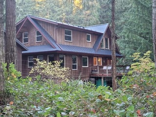 Deep Charcoal Interlock Slate aluminum roof on a brown two-storey chalet with a metal roof in a forest, Gabriola Island, British Columbia