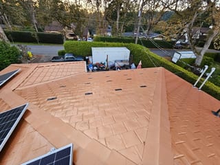 Copper Penny Interlock Slate aluminum roof being installed on a modern home with a metal roof among suburban trees, Victoria, British Columbia