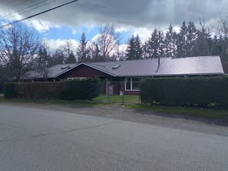 Tudor Brown Interlock Slate aluminum roof on a brown one-storey home with gable roof among tall trees, Duncan, British Columbia