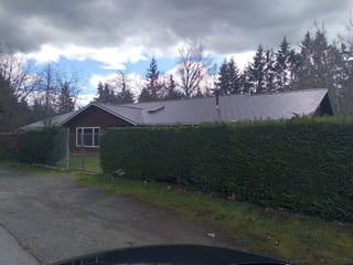 Tudor Brown Interlock Slate aluminum roof on a Tudor brown single-storey home among tall evergreens, Duncan, British Columbia