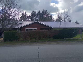 Tudor Brown Interlock Slate aluminum roof on a brown one-storey home with a metal roof among tall, Duncan, British Columbia