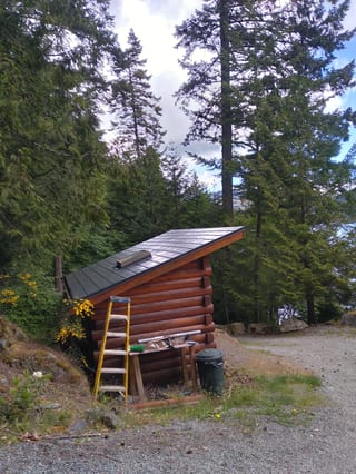 Deep Charcoal Interlock Slate aluminum roof on a brown log cabin with a metal roof among tall evergreens, Juan de Fuca, British Columbia