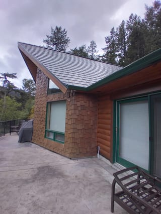 Deep Charcoal Interlock Slate aluminum roof on a brown single-storey chalet with green trim among tall, Juan de Fuca, British Columbia