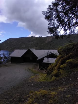Deep Charcoal Interlock Slate aluminum roof being installed on a dark home with a metal roof among trees and a lake, Juan de Fuca, British Columbia