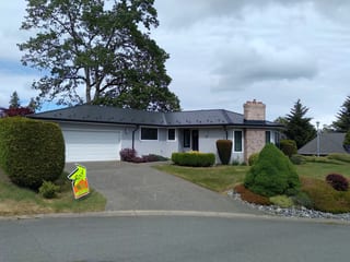 Black Interlock Slate aluminum roof on a white ranch home with a chimney among tall trees, Victoria, British Columbia