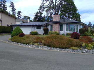 Black Interlock Slate aluminum roof on a two-storey home with dormers among tall trees and lush, Victoria, British Columbia