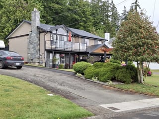 Black Interlock Slate aluminum roof on a beige two-storey home with a balcony among evergreens, Chemainus, British Columbia