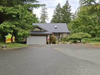 Black Interlock Slate aluminum roof on a beige home with a garage and dormers in a wooded setting, Duncan, British Columbia