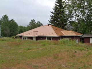 Copper Penny Interlock Slate aluminum roof on a red home with a copper penny metal roof among tall pines, Ladysmith, British Columbia