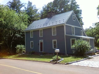 Two-story Colonial home in Northford, CT clad in blue-grey siding with a steep charcoal grey Interlock aluminum slate metal roof and brick chimney.