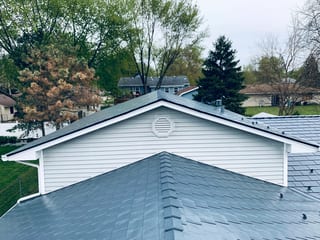 Deep Charcoal Interlock Slate aluminum roof on a white home with a metal roof among green trees, Elgin, Illinois