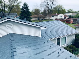 Deep Charcoal Interlock Slate aluminum roof on a white two-storey home with a metal roof among tall trees, Elgin, Illinois