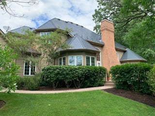 Deep Charcoal Interlock Slate aluminum roof on a tan two-storey home with dormers among tall trees and a, Crystal Lake, Illinois