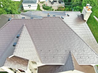 Colonial Brown Interlock Slate aluminum roof on a colonial-style home among tall trees in a suburban area, Calredon Hills, Illinois