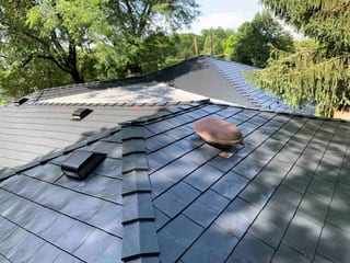 Black Interlock Slate aluminum roof on a black two-storey home with dormers among tall trees in a, Lombard, Illinois