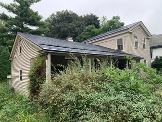 Black Interlock Slate aluminum roof on a beige house with a grey roof among tall trees, Woodstock, Illinois