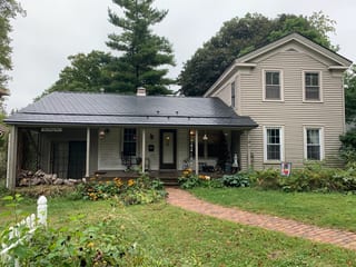 Black Interlock Slate aluminum roof on a tan two-storey farmhouse with a covered front porch among, Woodstock, Illinois