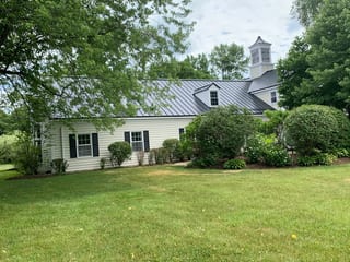 Black Interlock Standing Seam aluminum roof on a white Colonial home with dormers on a forested lakeside, Lake Forest, Illinois