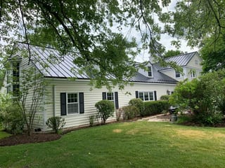 Black Interlock Standing Seam aluminum roof on a white house with a black metal roof among tall trees, Lake Forest, Illinois