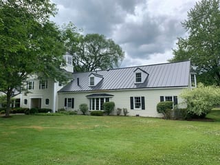 Black Interlock Standing Seam aluminum roof on a white colonial home with dormers among tall trees, Lake Forest, Illinois