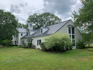 Black Interlock Standing Seam aluminum roof on a light green home with dormers among tall trees, Lake Forest, Illinois