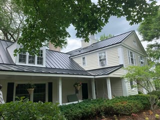 Black Interlock Standing Seam aluminum roof on a cream two-storey Colonial with dormers in a forested, Lake Forest, Illinois