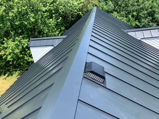 Black Interlock Standing Seam aluminum roof on a black metal roof on a modern home among tall green trees, Lake Forest, Illinois