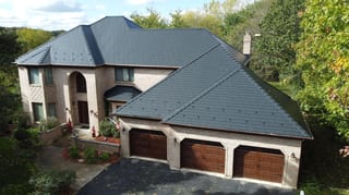 Black Interlock Slate aluminum roof on a beige two-storey colonial home among tall trees, Lemont, Illinois