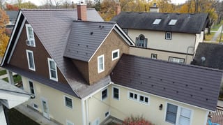 Colonial Brown Interlock Cedar Shingle aluminum roof on a tan two-storey Colonial home with dormers among tall trees, La Grange, Illinois